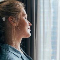 Morning daydreaming: profile of a beautiful blonde caucasian woman in blue pajamas sitting on bed and looking out of the window