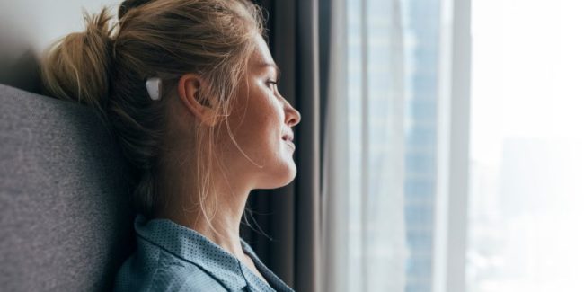 Morning daydreaming: profile of a beautiful blonde caucasian woman in blue pajamas sitting on bed and looking out of the window