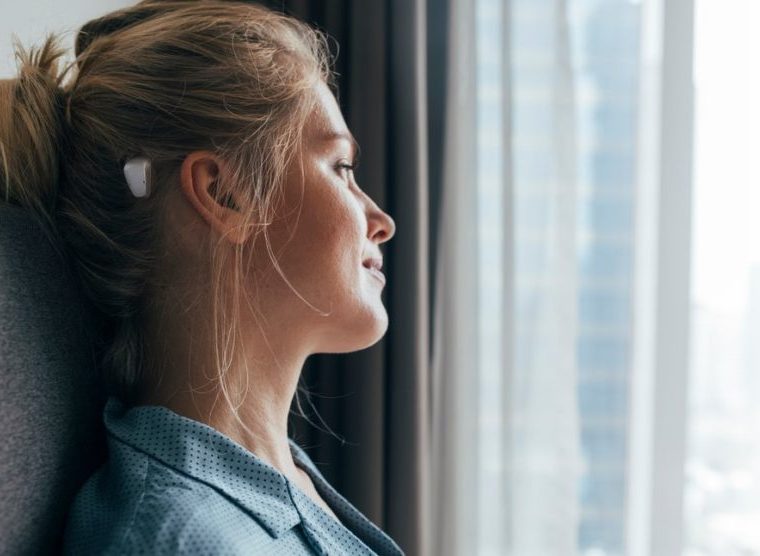 Morning daydreaming: profile of a beautiful blonde caucasian woman in blue pajamas sitting on bed and looking out of the window