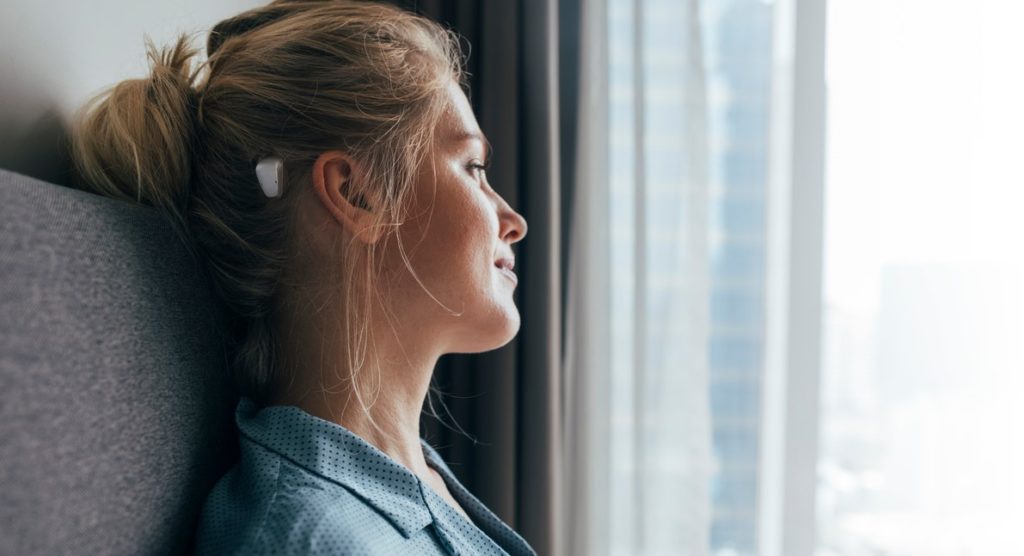 Morning daydreaming: profile of a beautiful blonde caucasian woman in blue pajamas sitting on bed and looking out of the window